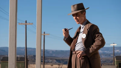 Cillian Murphy als Oppenheimer in einer trostlosen Landschaft, nachdenklich mit einer Pfeife in der Hand.