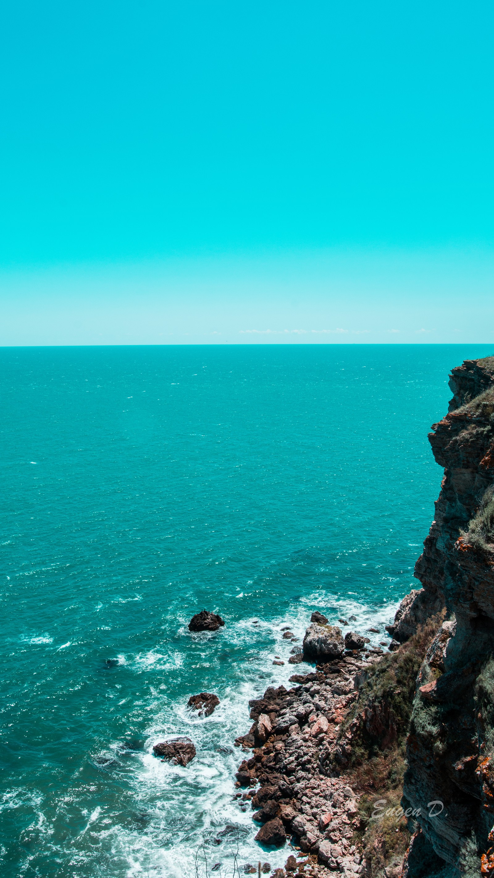 There is a man standing on a cliff overlooking the ocean (blue, blueocean, bluesea, clear, idle)