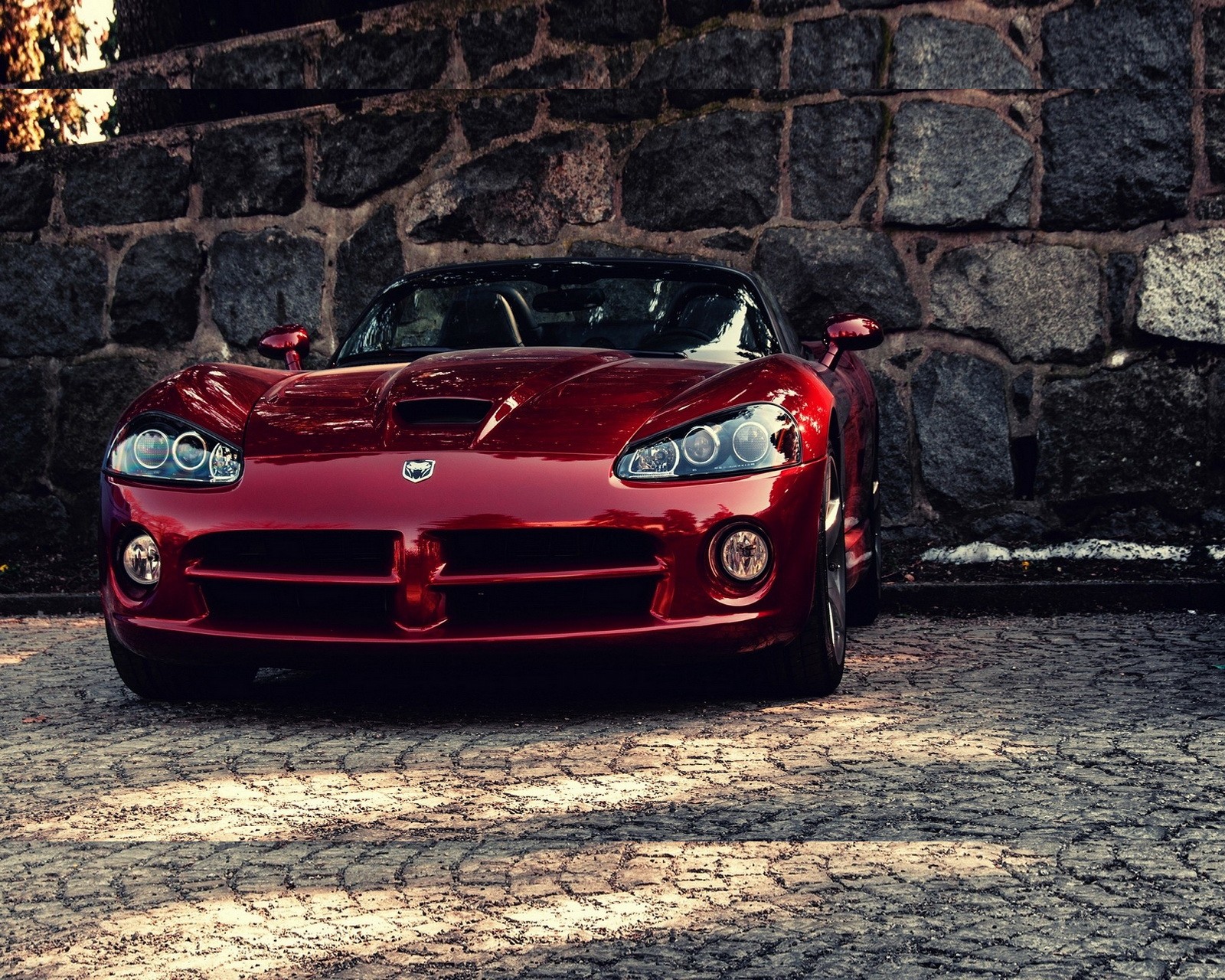 A close up of a red sports car parked in front of a stone wall (dodge viper, red)