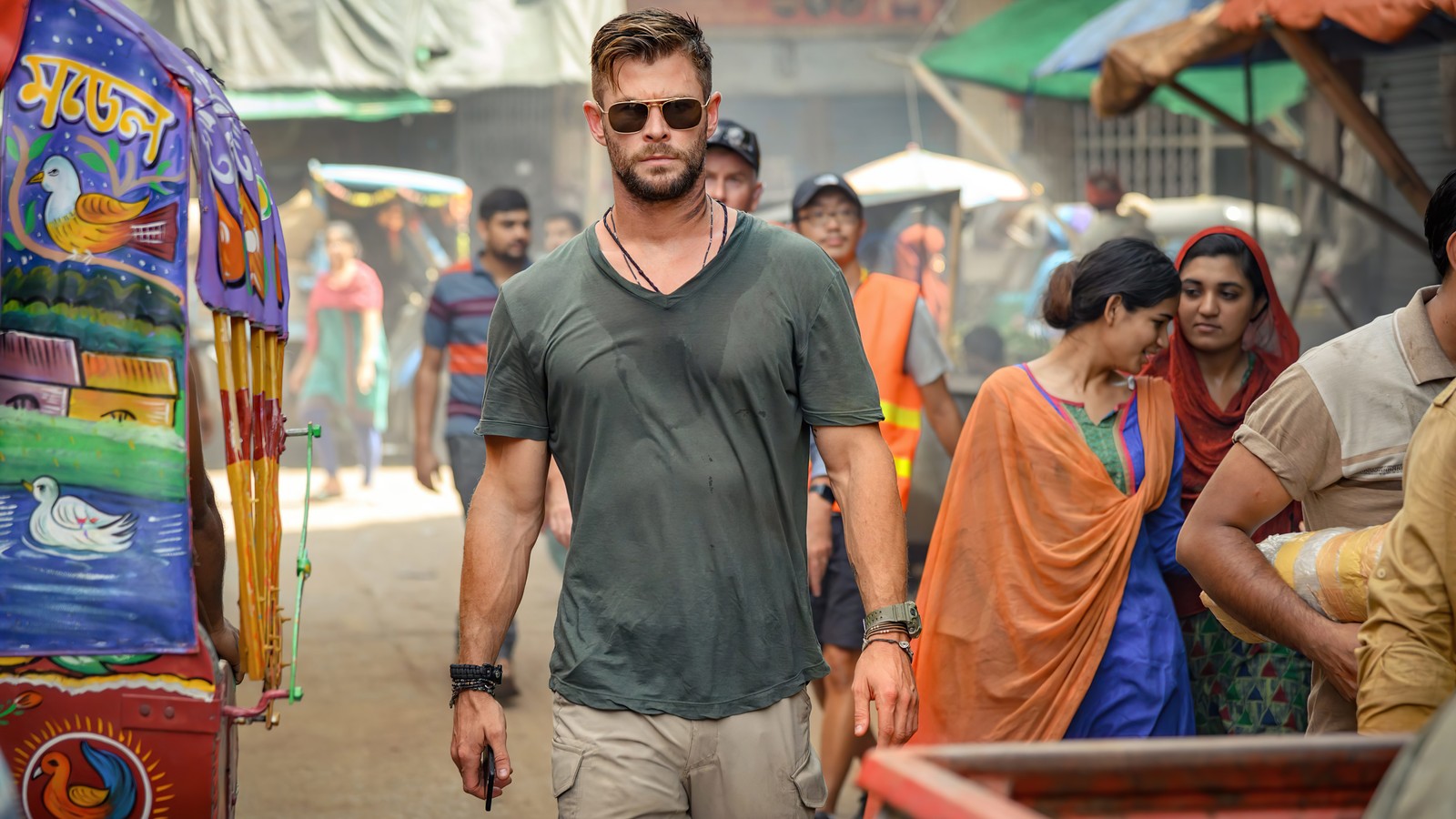 Uma imagem borrada de um homem caminhando por uma rua movimentada com um carrinho ao fundo (extração, filme, 2020, netflix, chris hemsworth)