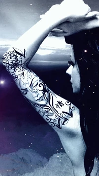 A woman with a beautifully detailed tattoo on her arm, gazing thoughtfully into the distance against a celestial backdrop.