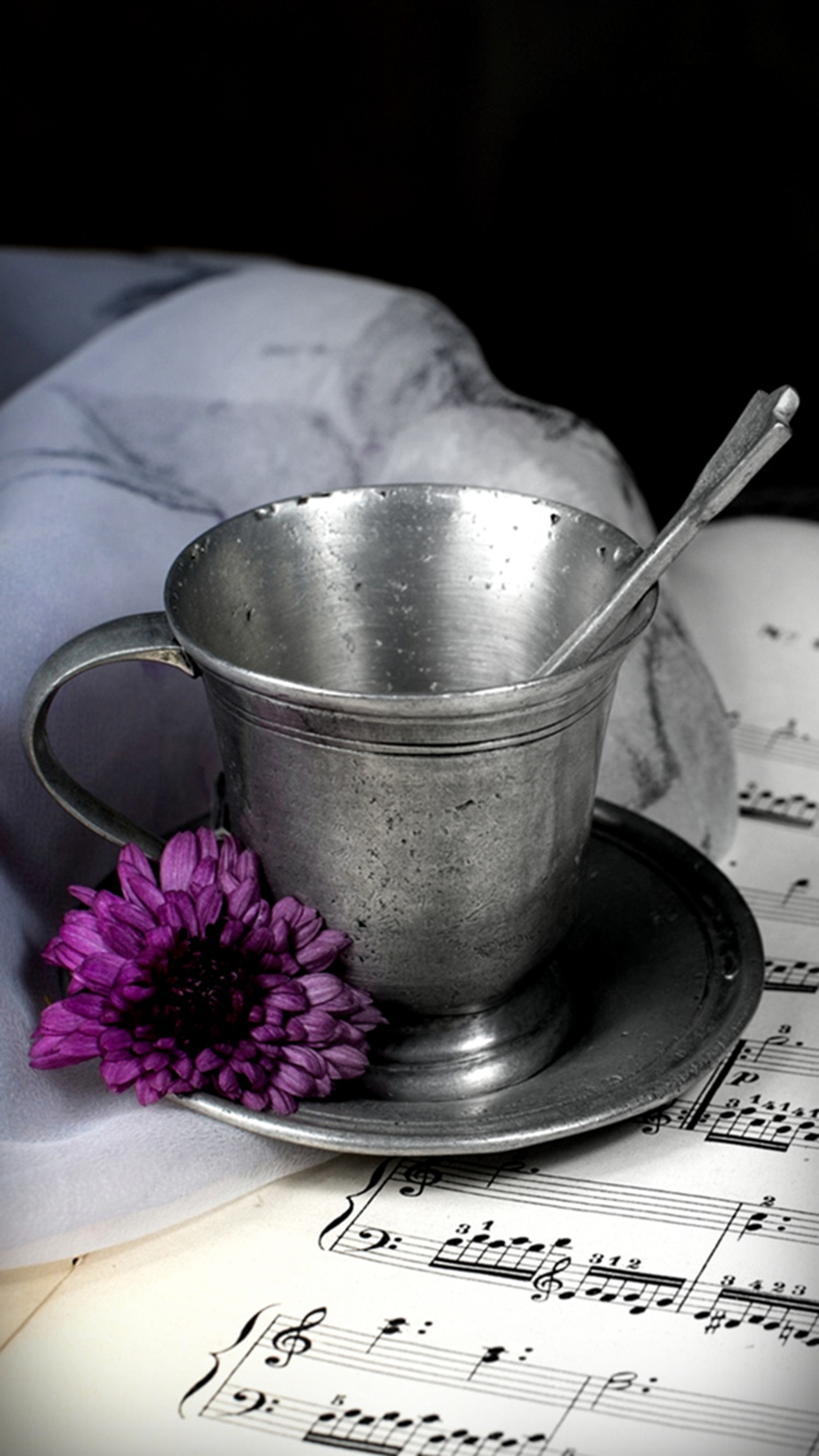 There is a silver cup and saucer on a sheet of music (flower, music, purple, romantic)