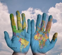 World Map Painted on Hands Against a Cloudy Sky