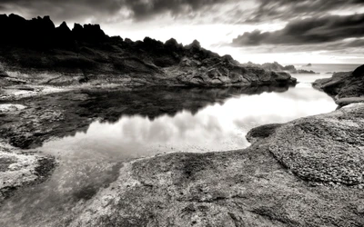 Paisaje costero en monocromo con reflejos en agua tranquila