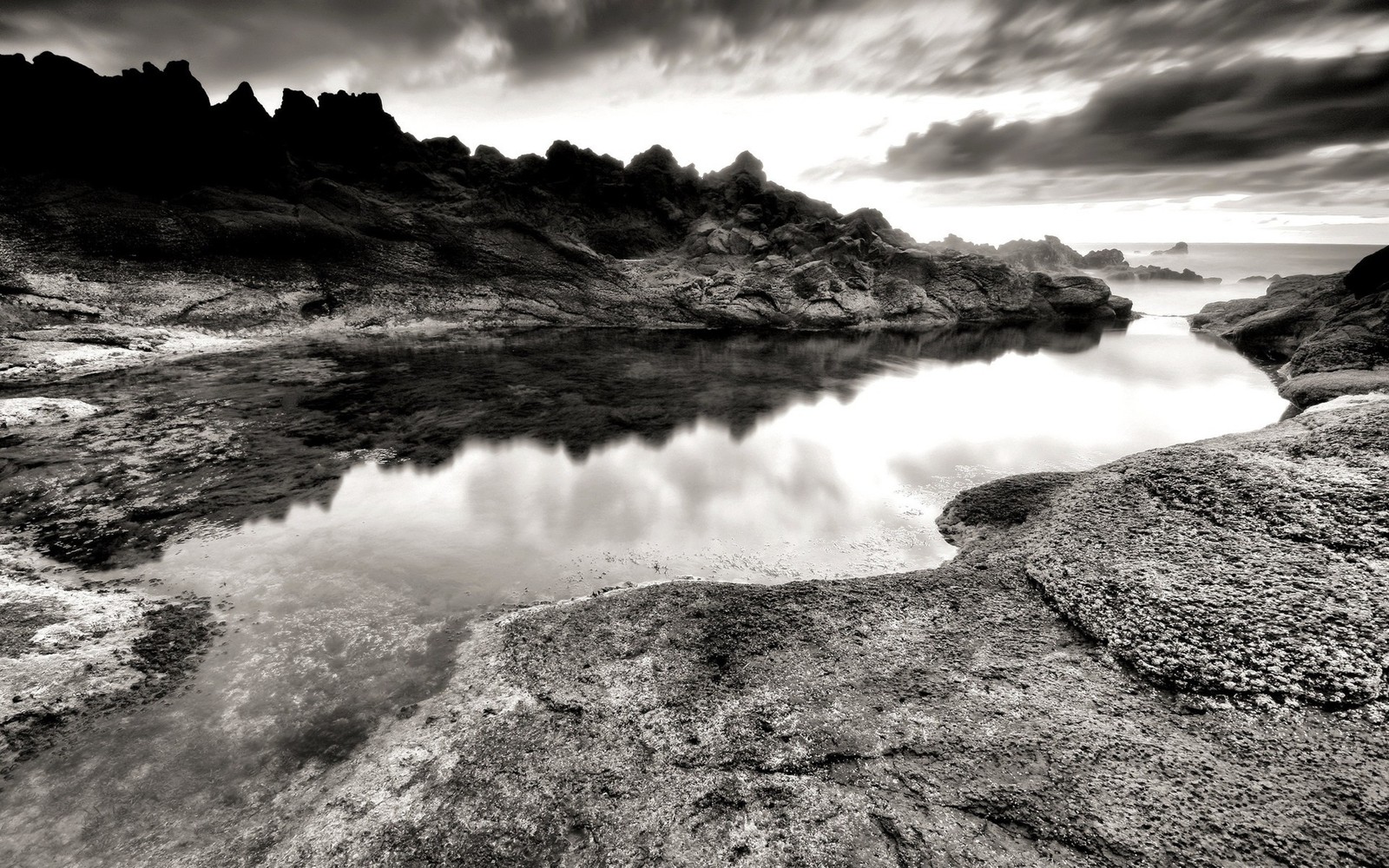 Arafed view of a body of water with rocks and a sky (black and white, nature, water, sea, rock)