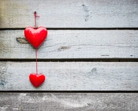 Two red heart ornaments hanging against a rustic wooden background.