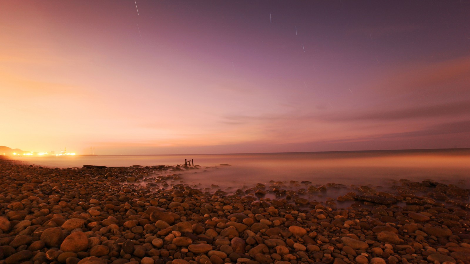 Il y a une vue d'une plage avec des rochers et quelques lumières (eau, plan deau, nuit, nature, la côte)