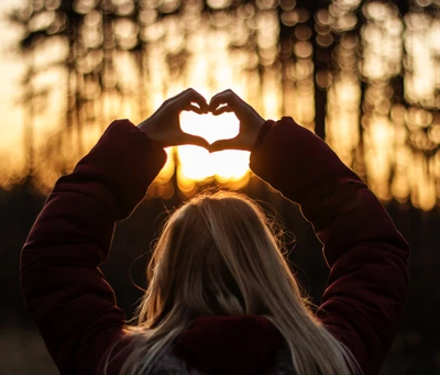 Silhouette d'une personne formant un cœur avec les mains contre un coucher de soleil, symbolisant l'amour et le bonheur dans la nature.