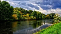 Ruhige Flussreflexion zwischen üppigem Grün und dramatischen Himmel