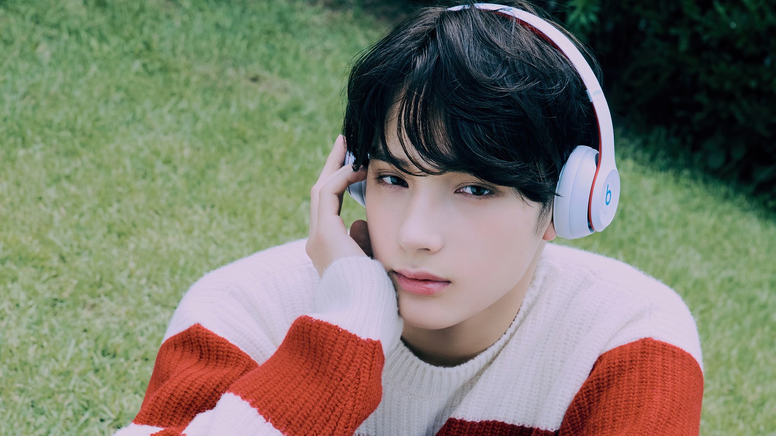 Un primer plano de una persona con auriculares en un campo de hierba (txt kpop, tomorrow x together, 투모로우바이투게더, kpop, k pop)