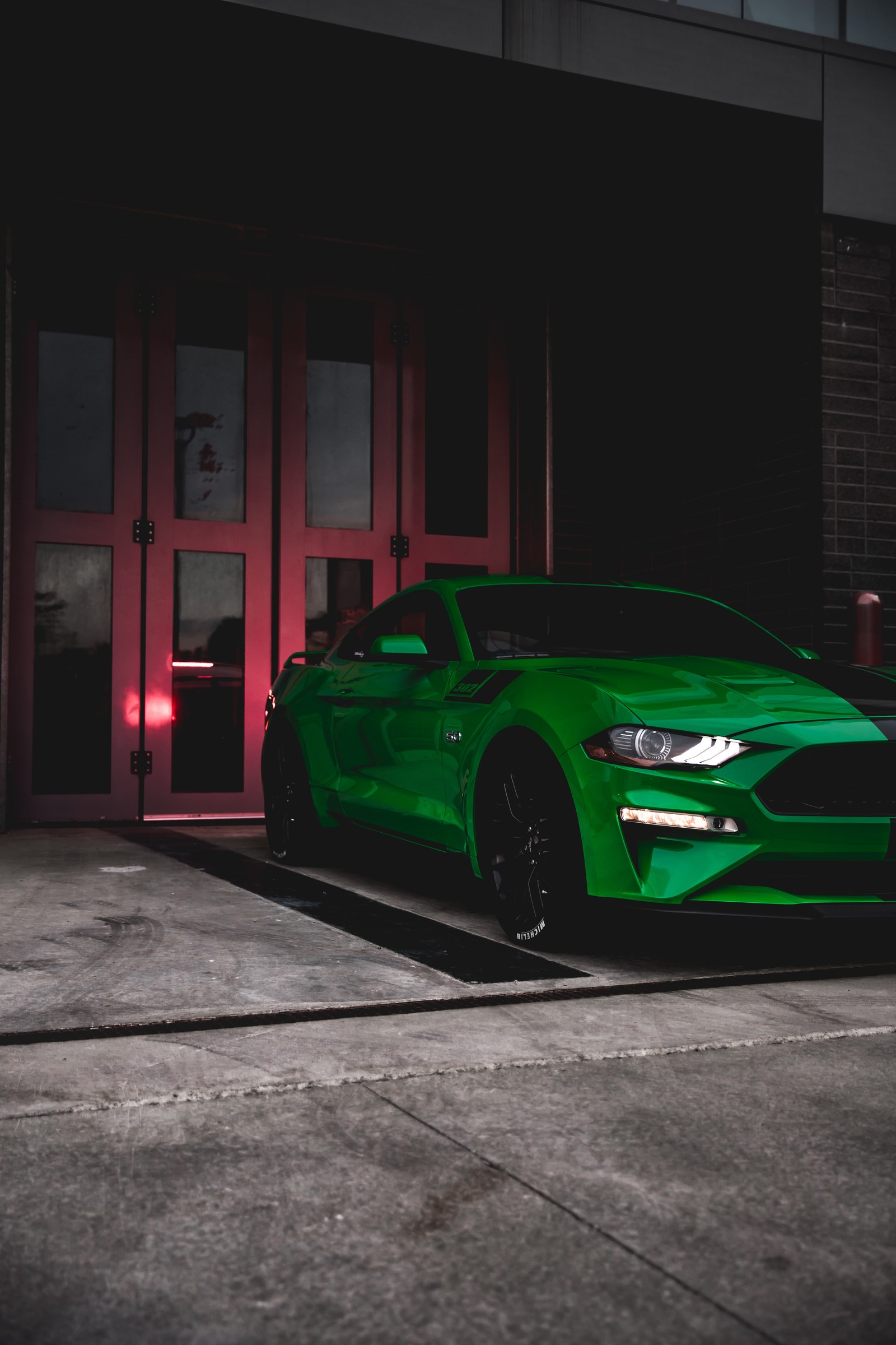 A close up of a green car parked in front of a building (car, sports car, green, rim, wheel)