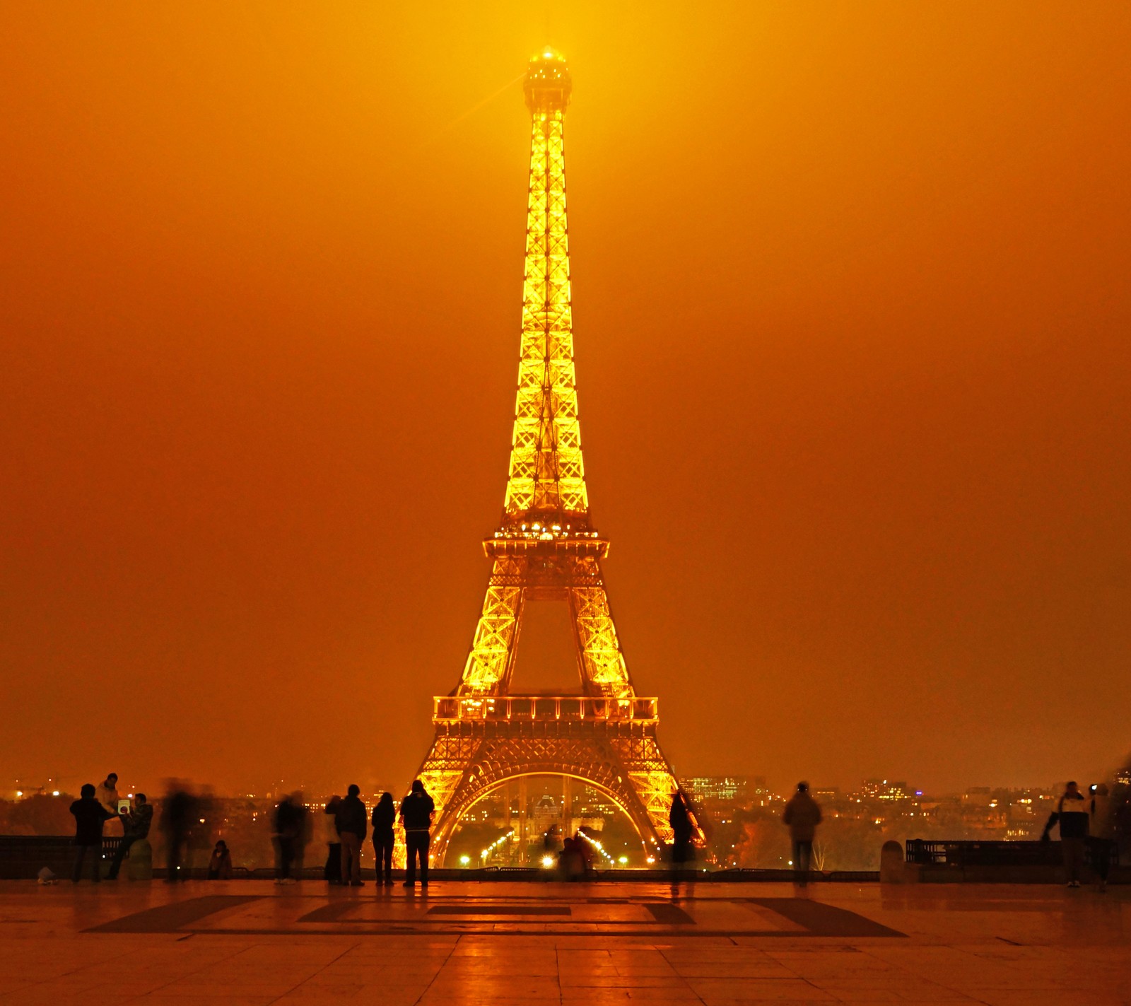 Araffe view of the eiffel tower at night with people standing around (eiffel, france, night, paris, place)