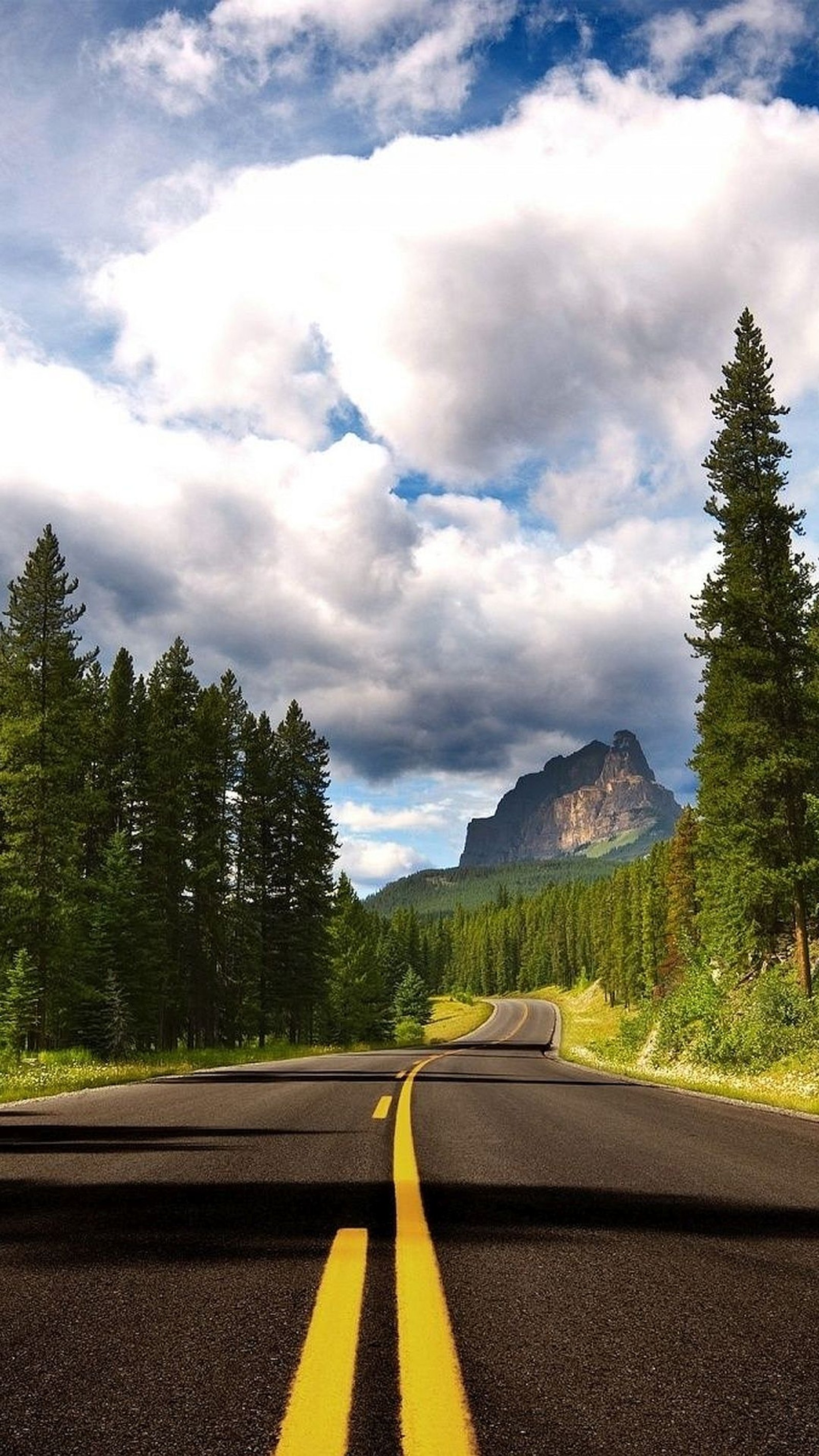 There is a road with two yellow lines going through the middle (beautiful drive, mountains, road, sky, trees)