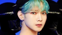 Yeosang von ATEEZ mit auffälligen blauen Haaren und fesselndem Blick vor einem dramatischen Hintergrund.