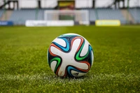 A close-up of a colorful soccer ball resting on vibrant green artificial turf at a football pitch.