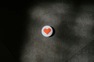 Gros plan d'un bouton rond avec un symbole de cœur orange sur un fond sombre texturé.