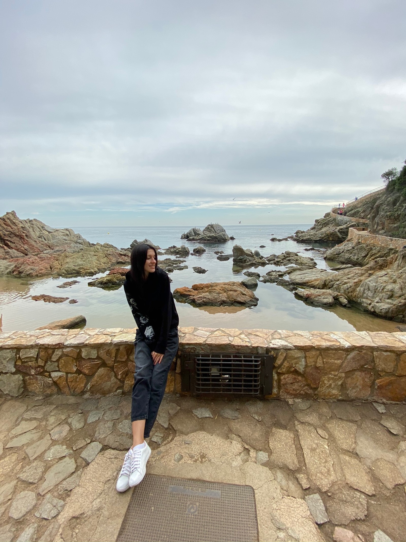 Une femme assise sur un mur de pierre près de l'eau (voyage, tourisme, eau, denim, jeans)