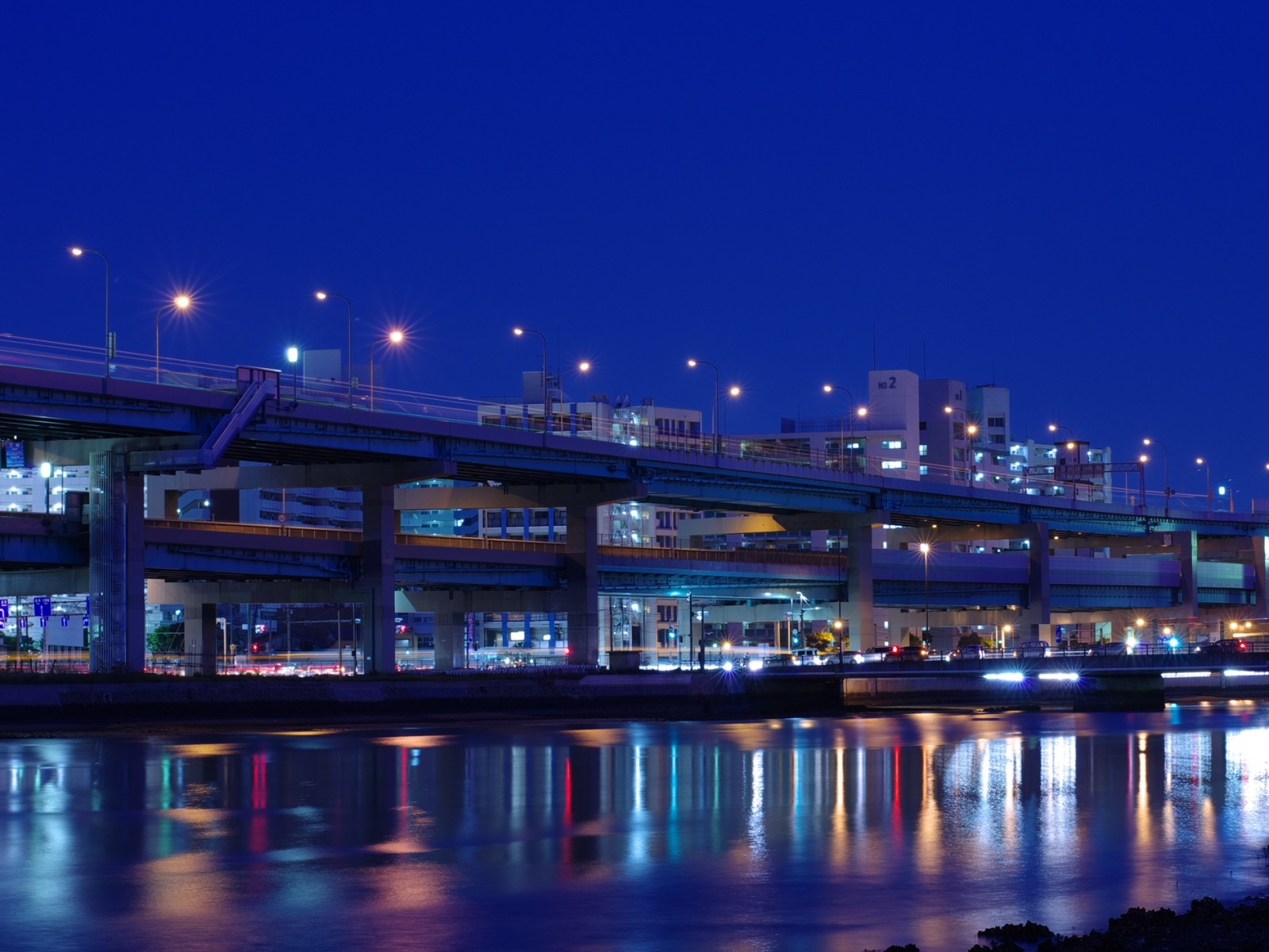 Vista noturna de uma ponte sobre um rio com uma cidade ao fundo (noite, azul, ponte, reflexo, cidade)