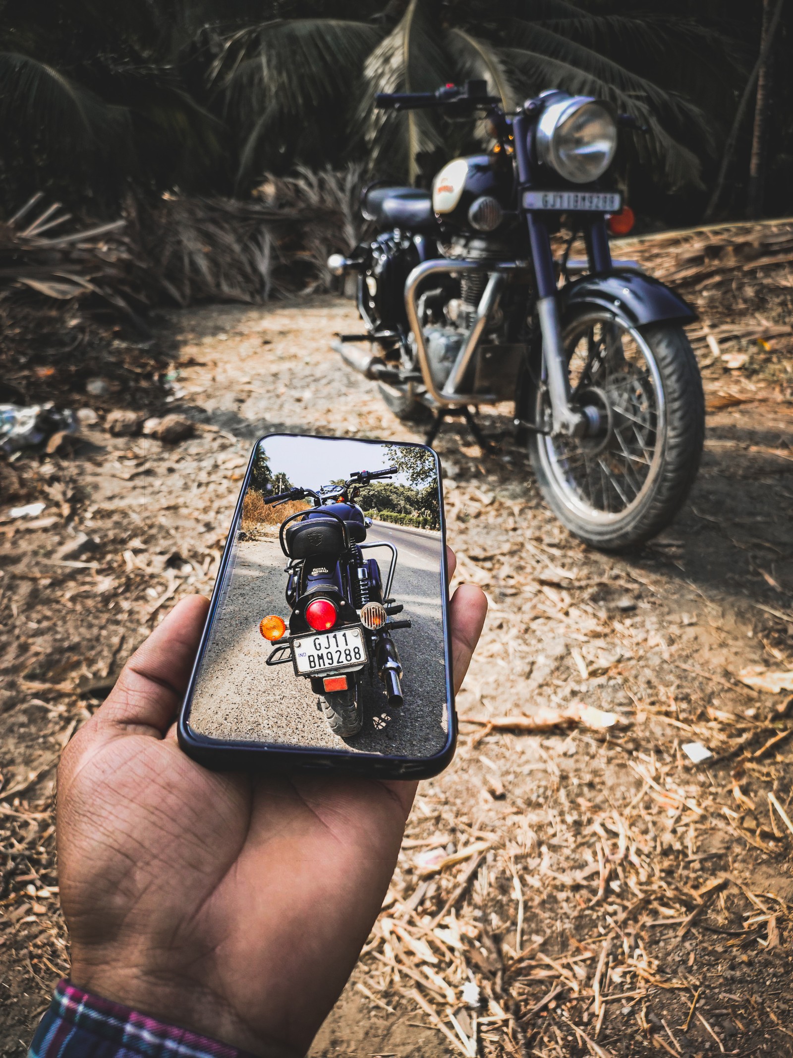 Someone holding a phone up to a picture of a motorcycle (bike, bullet, royal enfield)