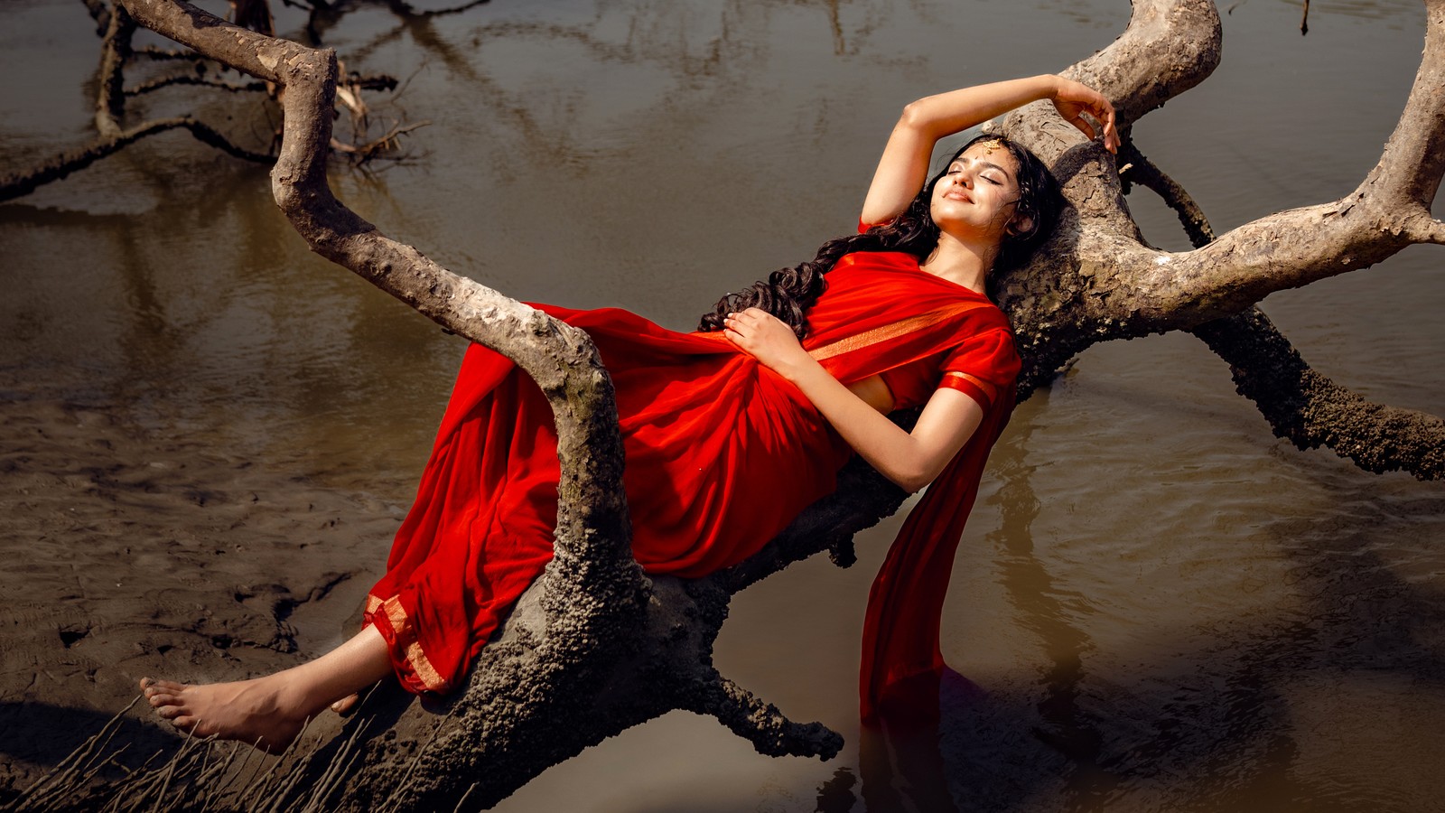 Mujer árabe en vestido rojo recostada sobre una rama de árbol en el agua (mamitha baiju, estética roja, actriz malayalam, actriz india, sari)