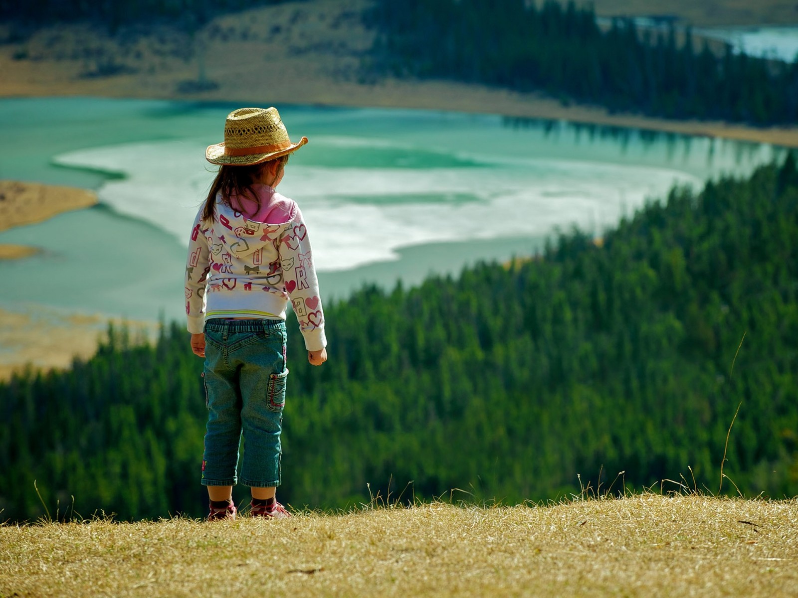 There is a little girl standing on a hill looking at a lake (fun, happiness, rural area, fields, prairie)