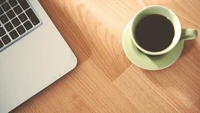 Tasse de café à côté d'un MacBook sur un sol en bois