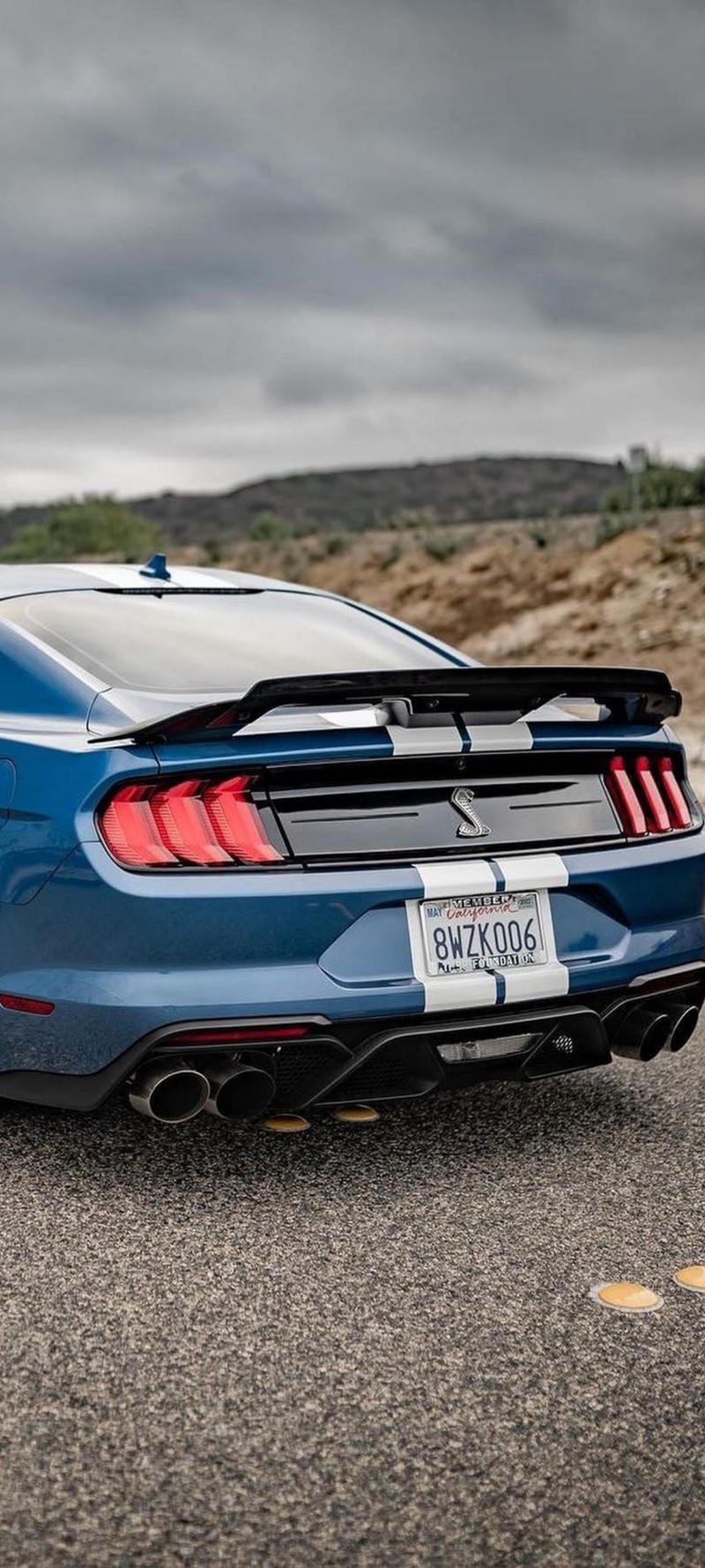 Gros plan d'une mustang bleue garée sur une route (voitures, pneu, nuage, éclairage automobile)