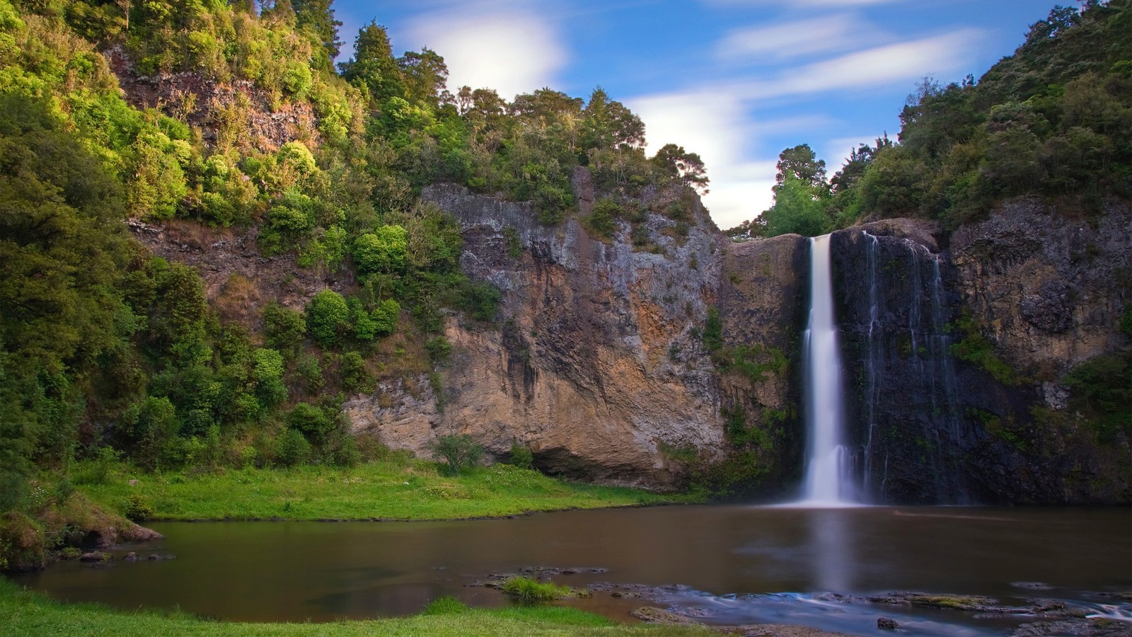 A large waterfall in a lush green forest next to a river (waterfall, body of water, water resources, nature, water)