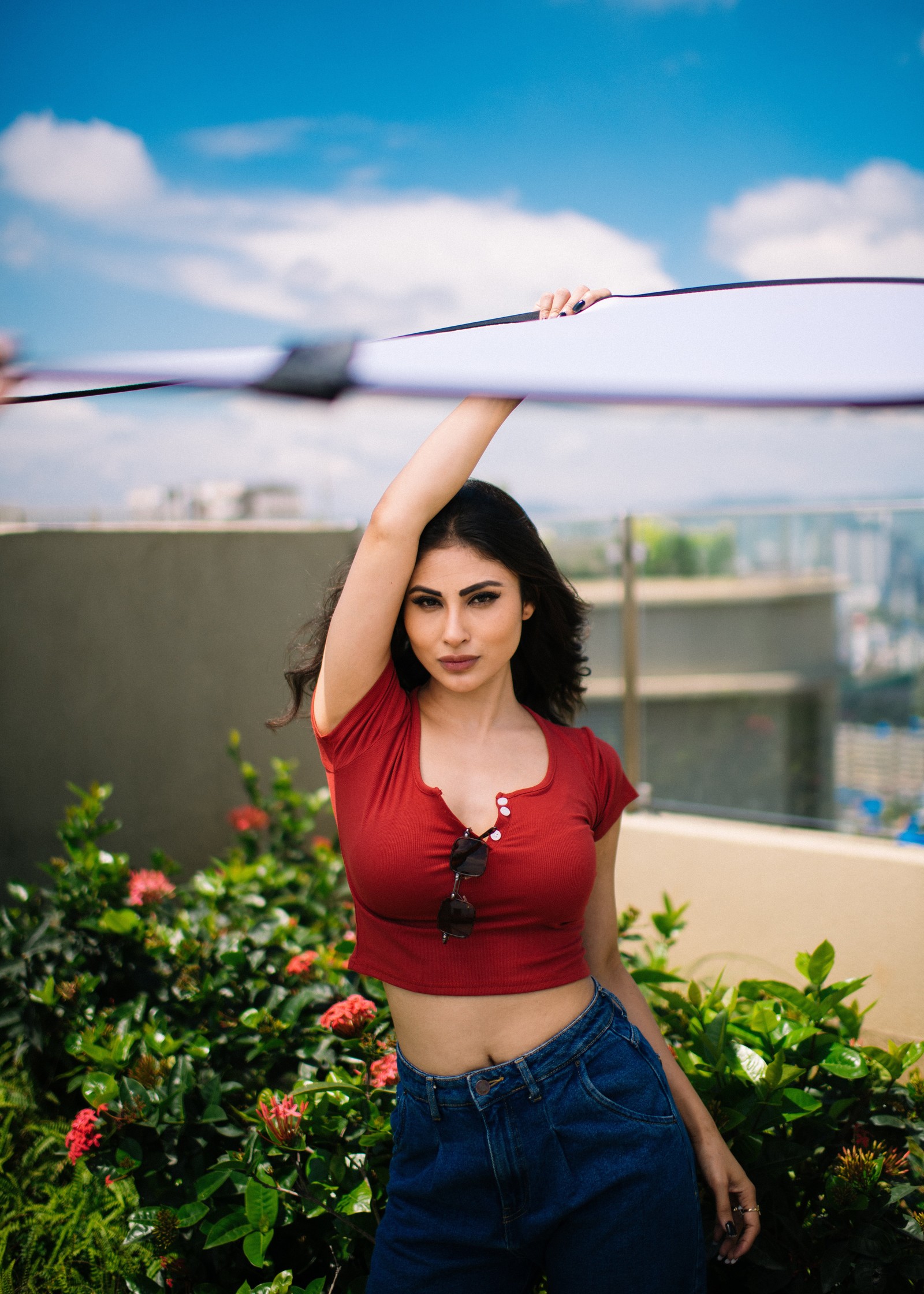 Una mujer árabe con una camisa roja sosteniendo una tabla de surf sobre su cabeza (mouni roy, 5k, actriz india, actriz de bollywood, gente)