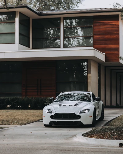 Elegante coche deportivo Aston Martin blanco aparcado frente a una casa arquitectónica moderna, mostrando lujo y elegancia de diseño.