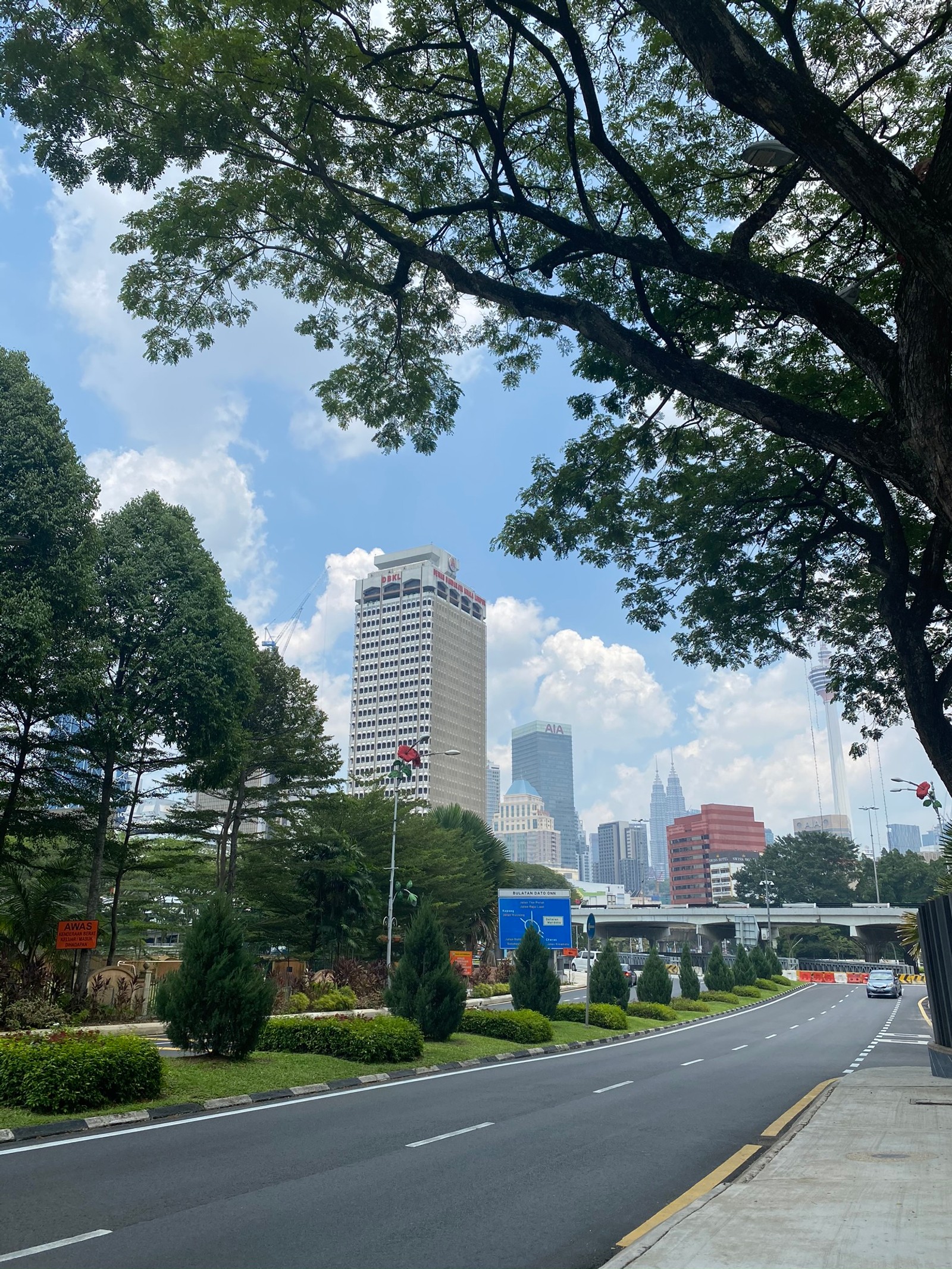 Es gibt eine straße mit einem baum und einem gebäude im hintergrund (kuala lumpur, straße, gewässer, natur, hochhaus)