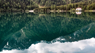 Lago de montanha sereno com reflexos de árvores e uma casa