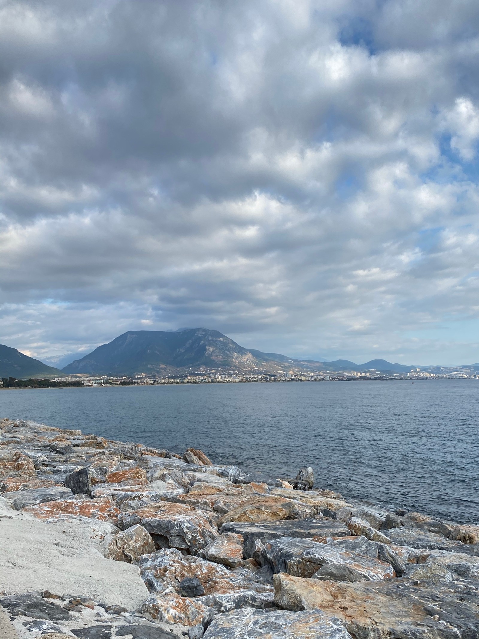 There is a man sitting on a bench on the beach (sea, cloud, water, water resources, mountain)