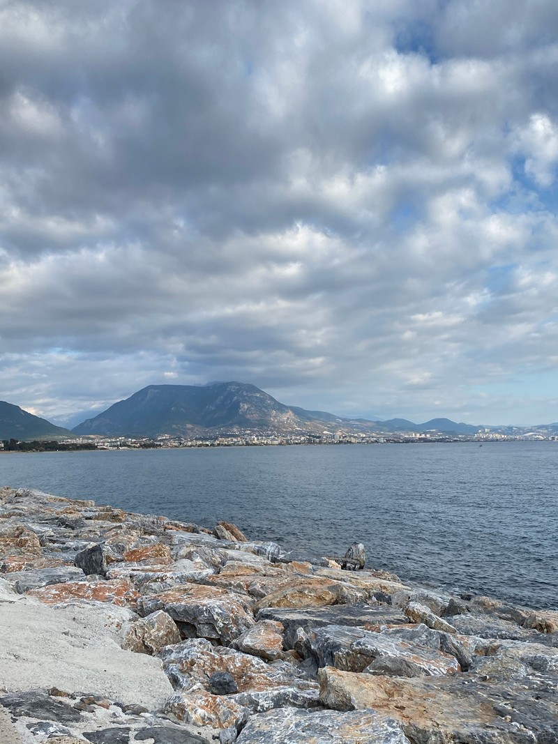 На скамейке на пляже сидит мужчина (море, облако, вода, водные ресурсы, гора)