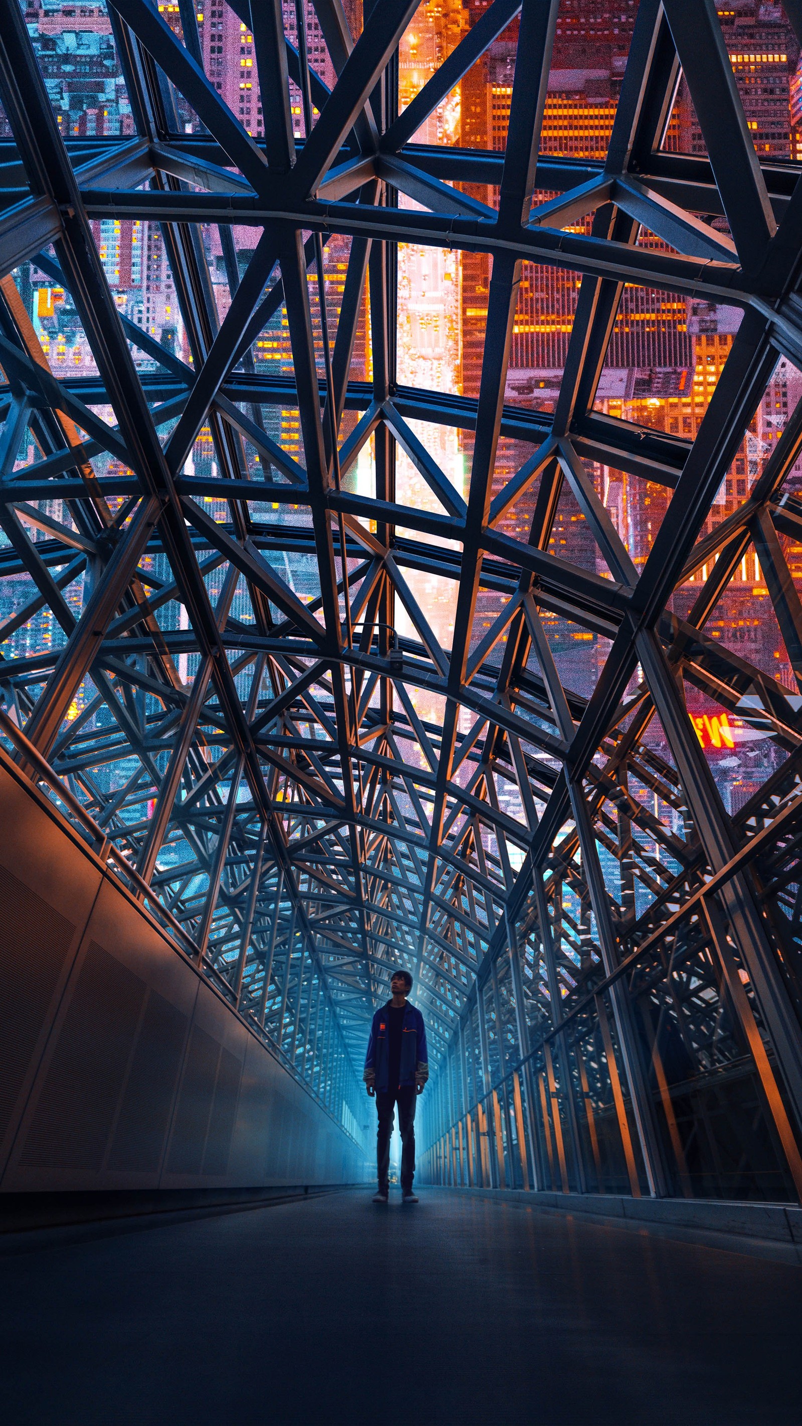 There is a man walking down a walkway in a city at night (landmark, light, infrastructure, triangle, building)