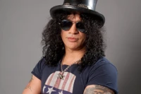 Stylish musician with long curly hair, wearing a black top hat and sunglasses, embodying rock fashion.