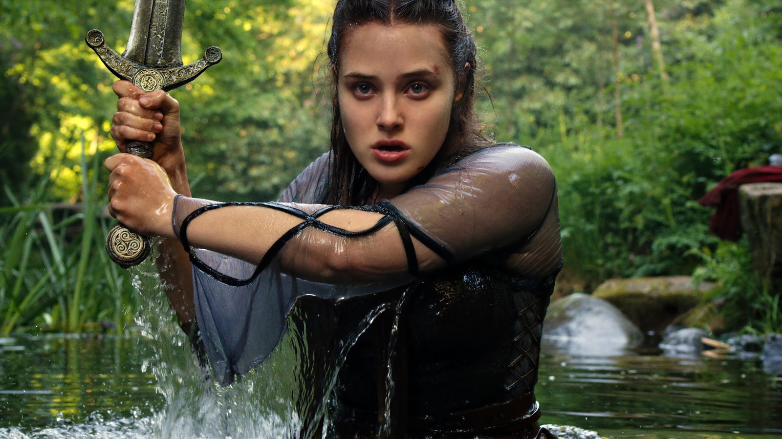 Une femme arabe en combinaison de plongée tenant une épée dans une rivière (netflix maudit, série télévisée, nimue, katherine langford)