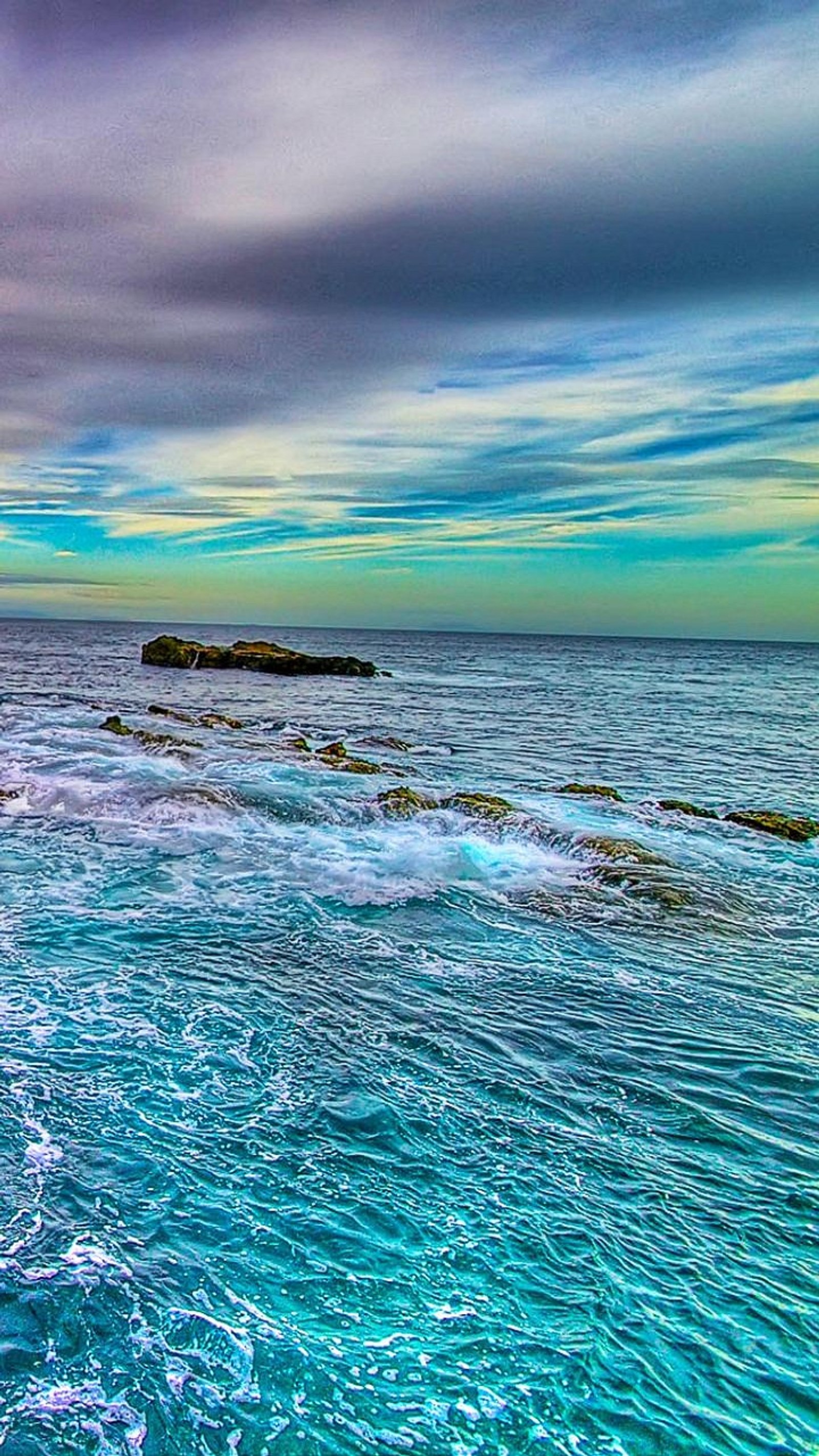 Des surfeurs sur les rochers d'une plage rocheuse sous un ciel nuageux (incroyable, amazing sea view, coloré, nature, mer)