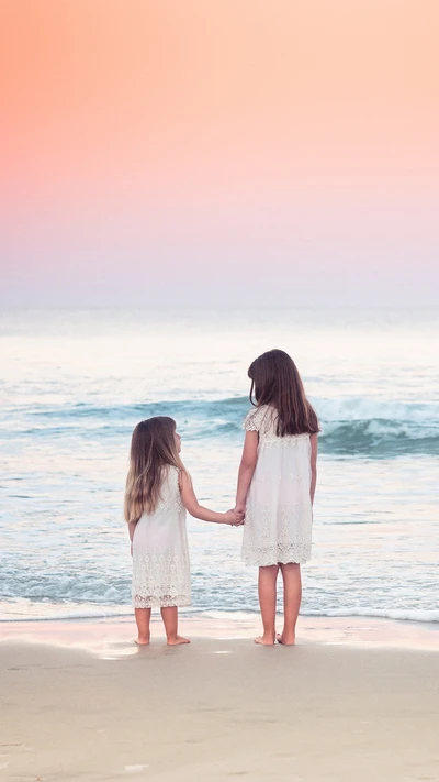 Deux petites filles se tenant par la main sur la plage au coucher du soleil