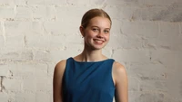 Angourie Rice sonriendo contra una pared blanca texturizada