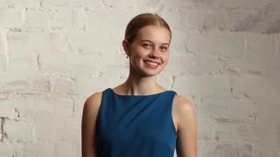 Angourie Rice souriant contre un mur blanc texturé