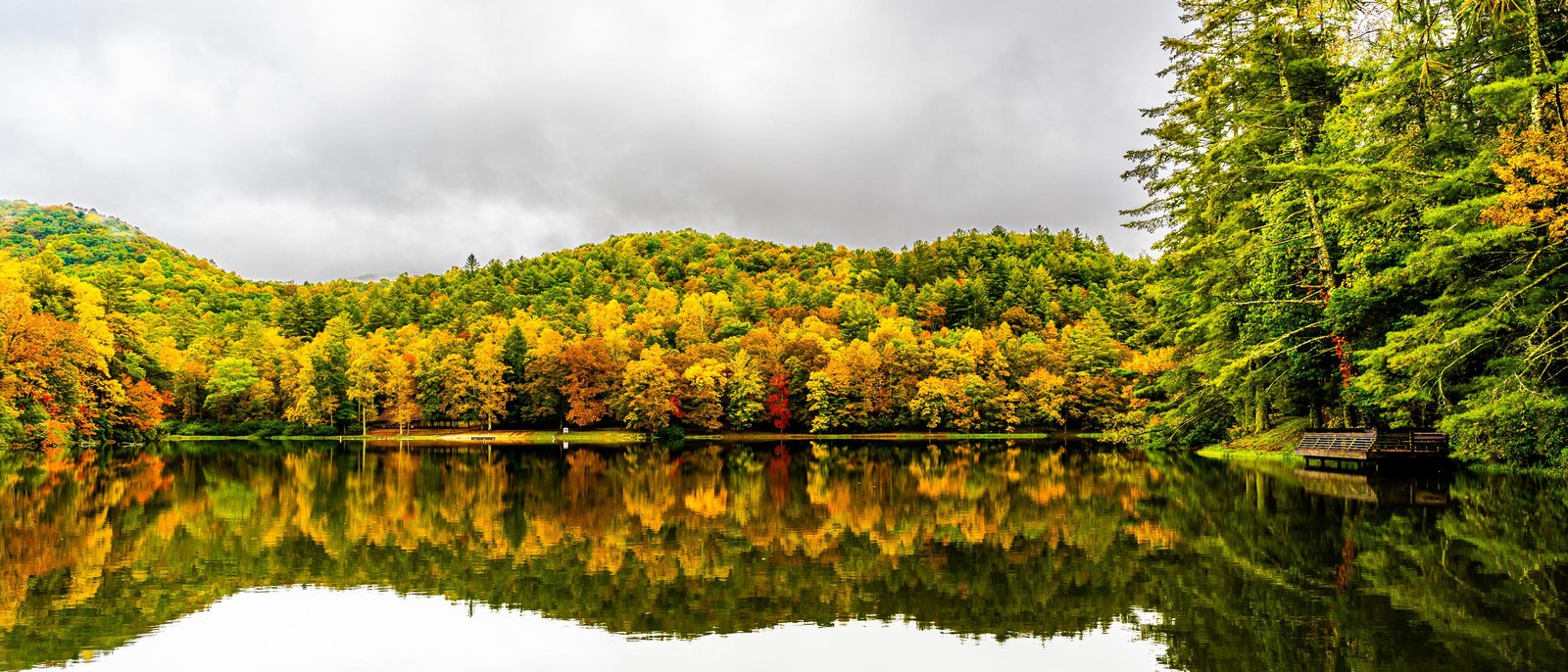 Una vista de un lago rodeado de árboles con follaje de otoño (reflexión, vegetación, humedal, nube, agua)