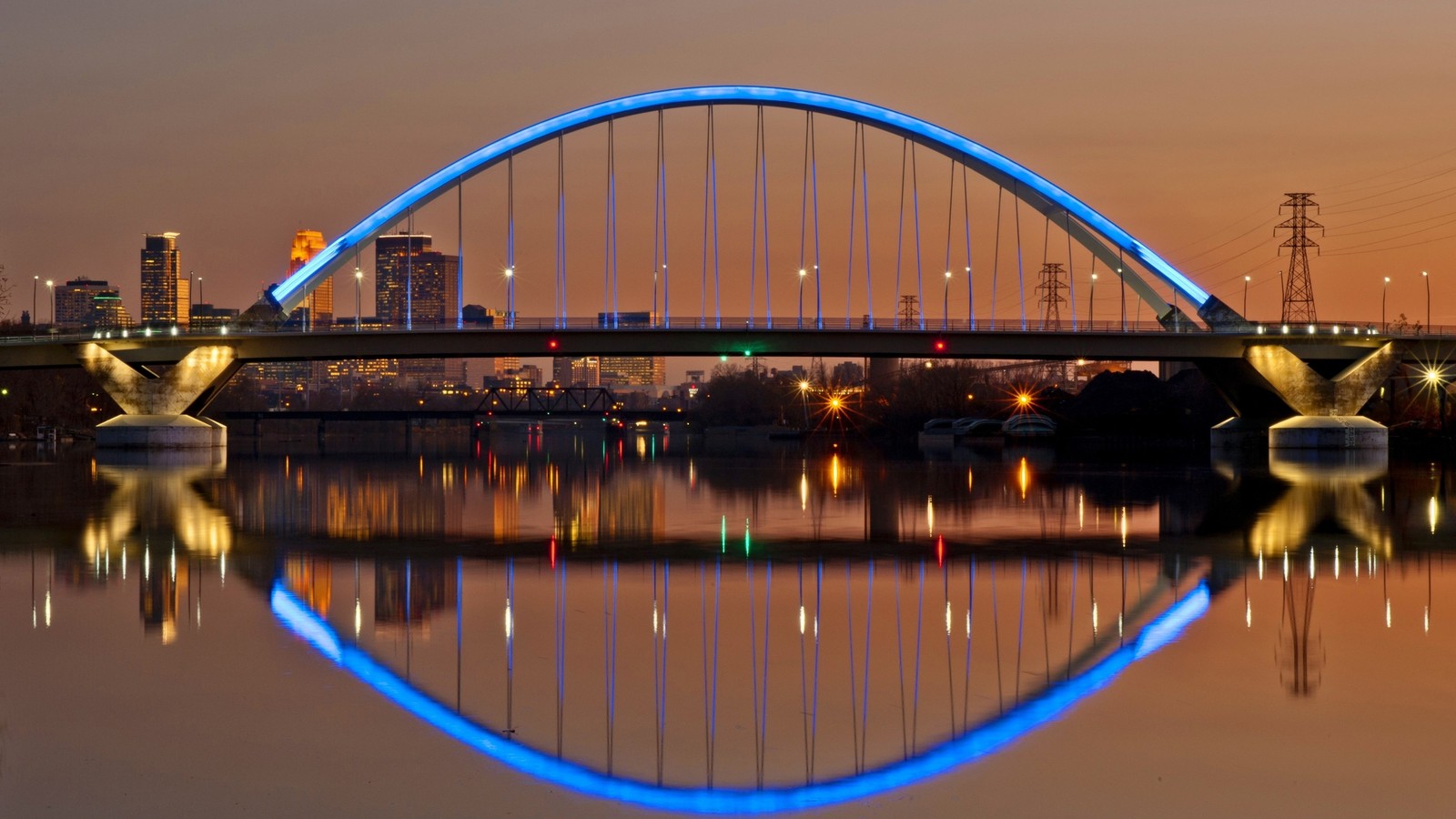 Un puente sobre un río con luz azul reflejándose en el agua (reflexión, minneapolis, puente, noche, agua)