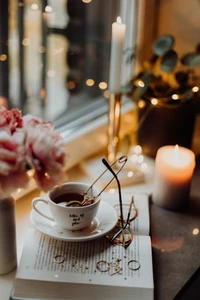 Moment de café confortable avec une tasse de thé, des fleurs et une douce lumière de bougie.