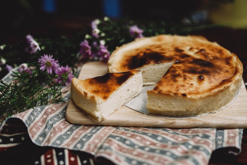 На разделочной доске лежит чизкейк с отсутствующим куском (чизкейк, десерт, блюдо, еда, кухня)