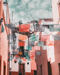 Des bannières en papel picado colorées pendent dans une ruelle urbaine, mêlant des motifs vibrants à des éléments architecturaux contemporains.