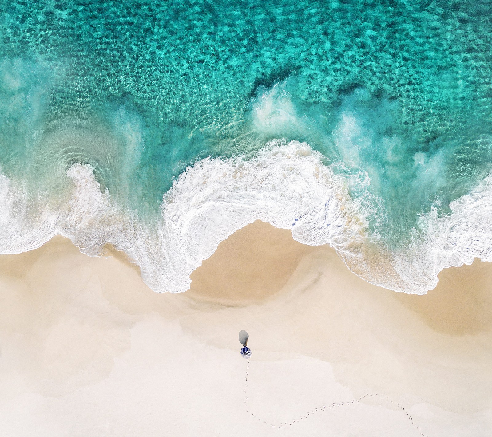 Vue aérienne d'une personne marchant sur une plage avec une planche de surf (android, pomme, ios, iphone, papier peint de stock)