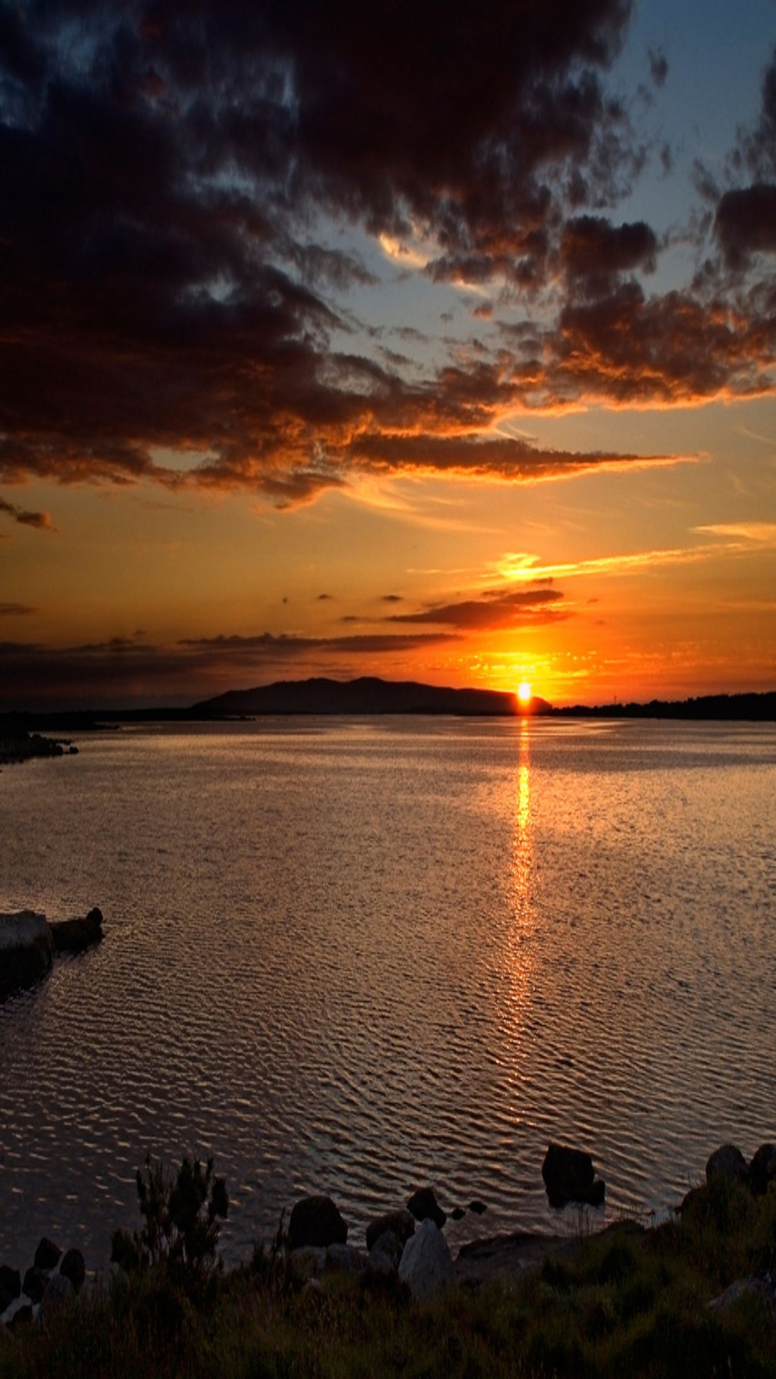 Pôr do sol sobre um lago com um barco na água e algumas pedras na água (praia, paisagem, natureza, por do sol)