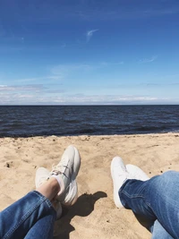 Relaxing by the Shore: A Beach Scene with Denim-Clad Feet