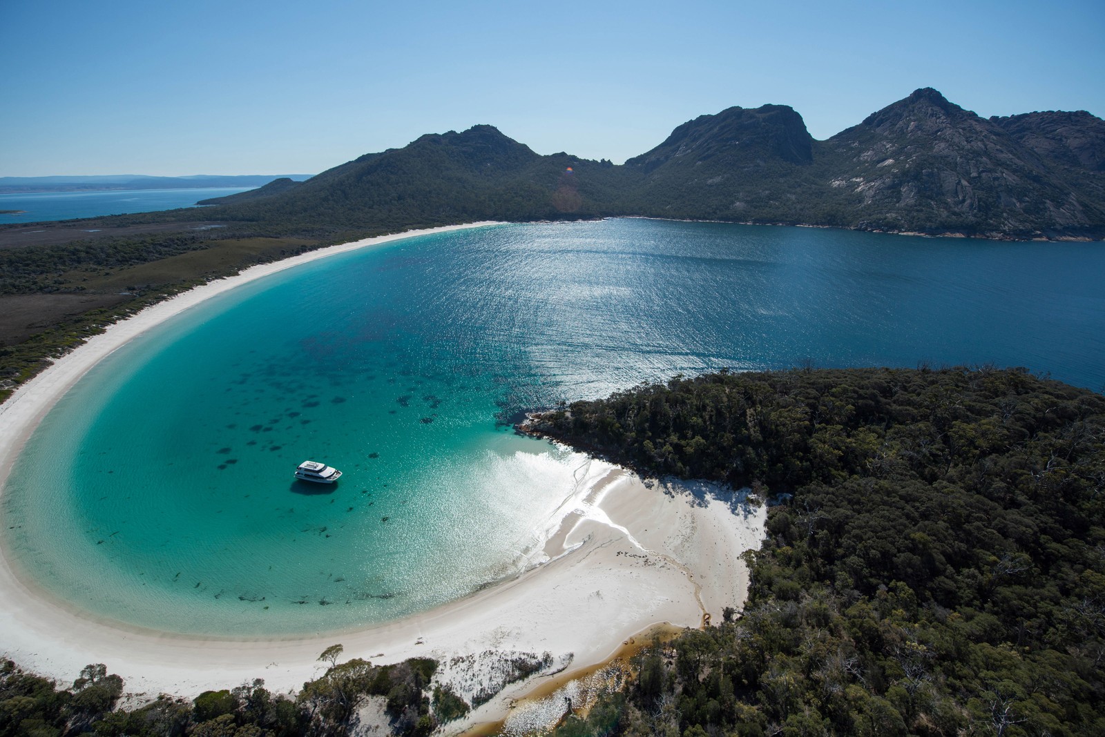 Uma vista de um barco em uma praia de areia branca perto de uma montanha (corpo de água, costa, mar, baía, formas costeiras e oceânicas)